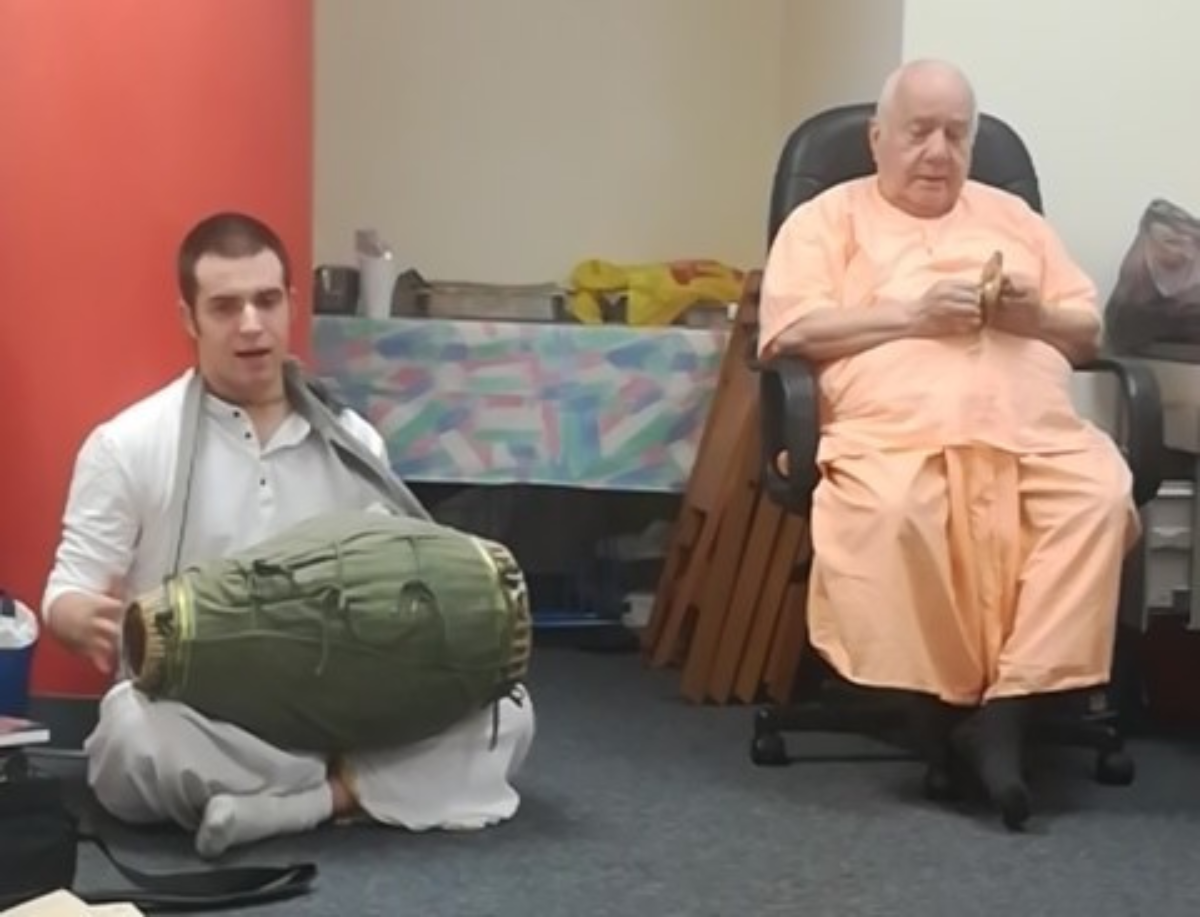 Krishna Keshava Das playing a mridanga drum beside Dr. B. Madhava Puri